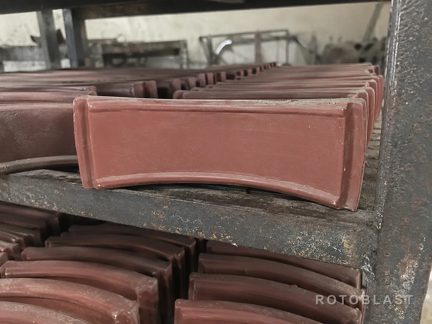 New upper wear liners stacked on the racks at Rotoblast's works — curved plates in primer, each one a bolt-in panel for the roof of a blast chamber.