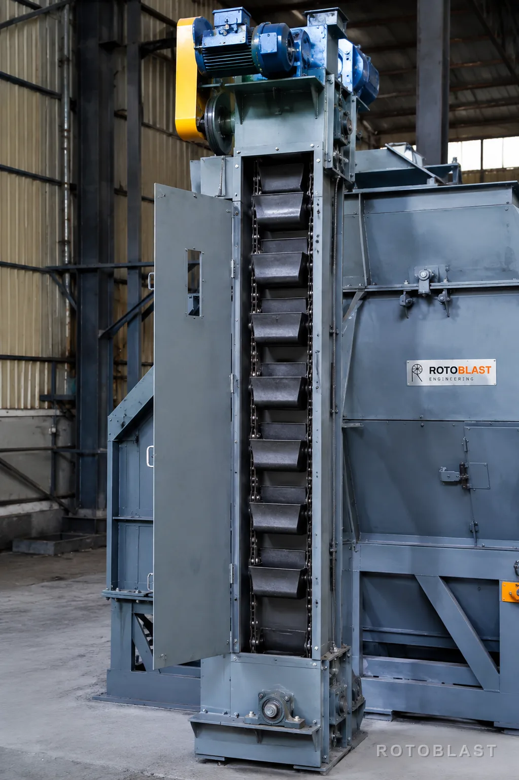Rotoblast bucket elevator lifting abrasive alongside a shot blasting machine cabinet